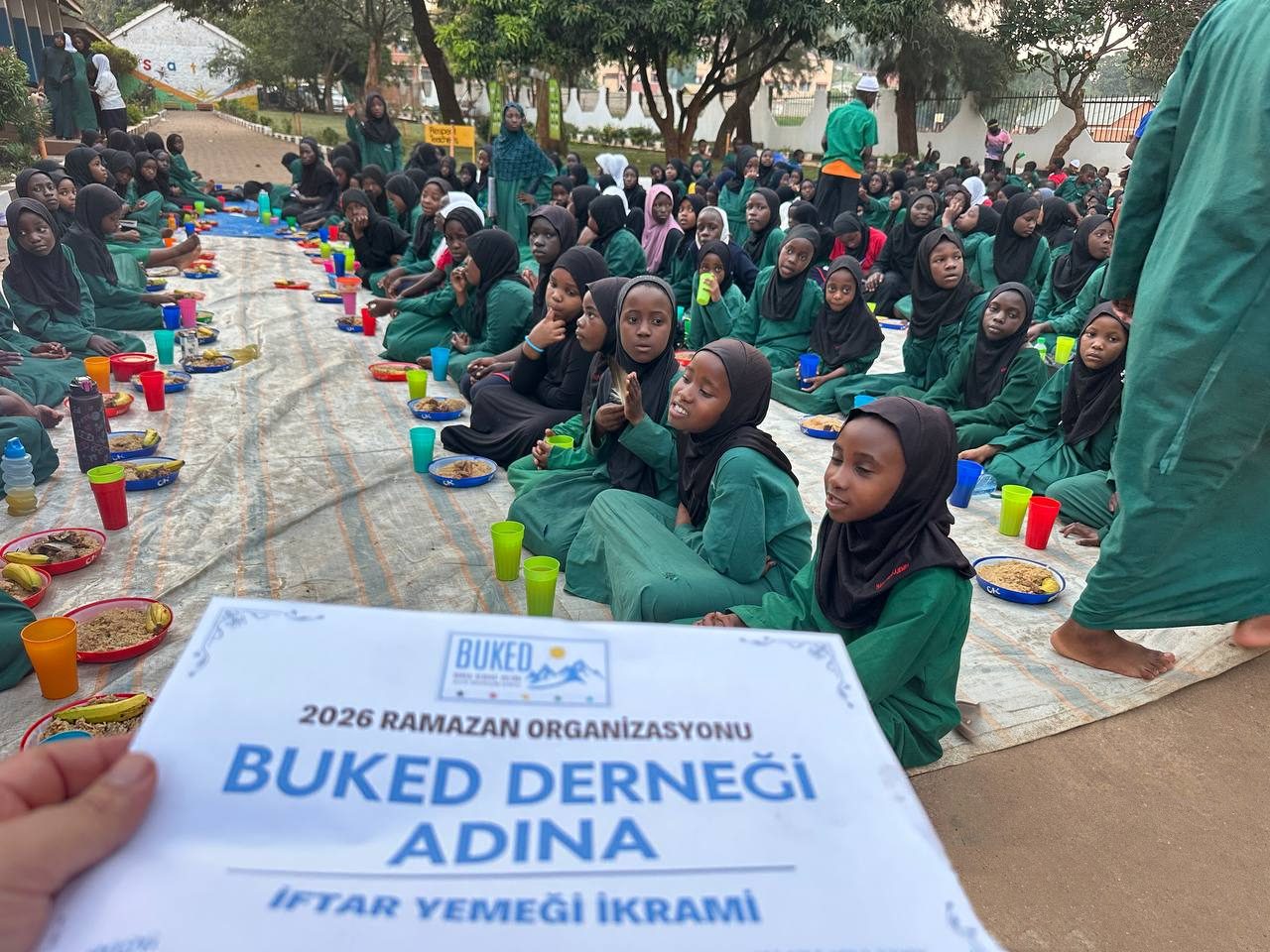 Afrika'da yerde sıra sıra oturmuş, iftar yemeğini bekleyen bir grup çocuk