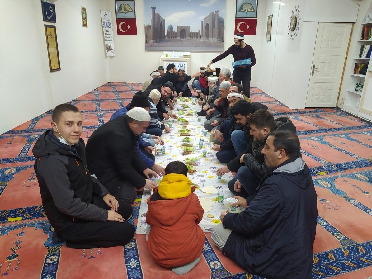 Salonda uzun bir sofra etrafında toplanmış kalabalık bir iftar