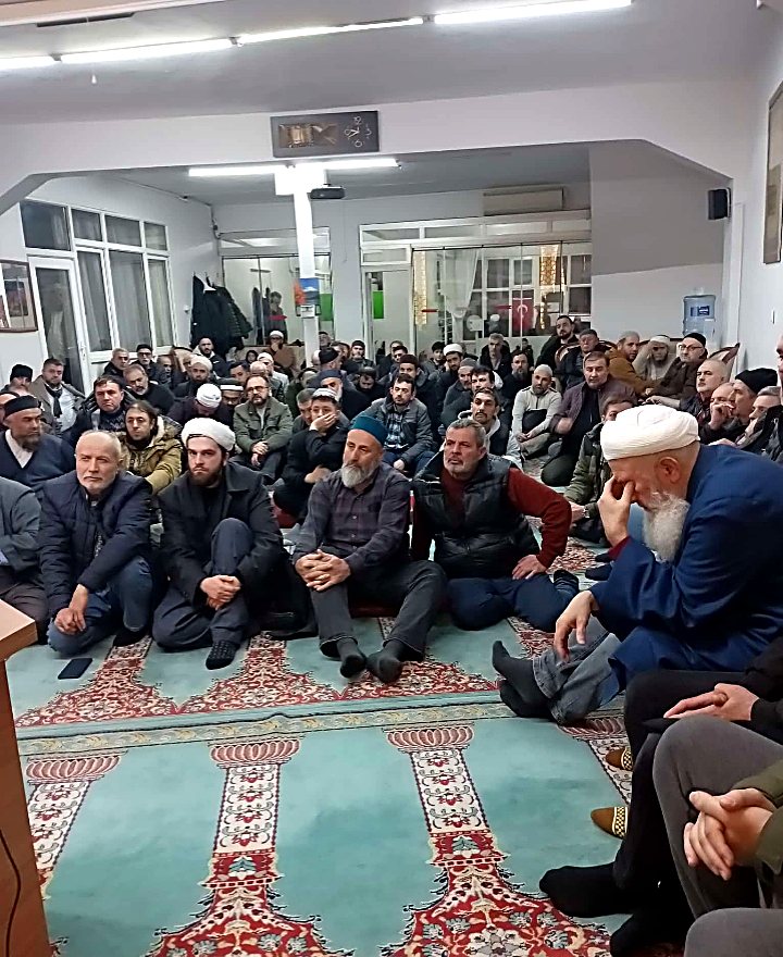 Geniş bir salonda kalabalık bir cemaate hitap eden bir hoca